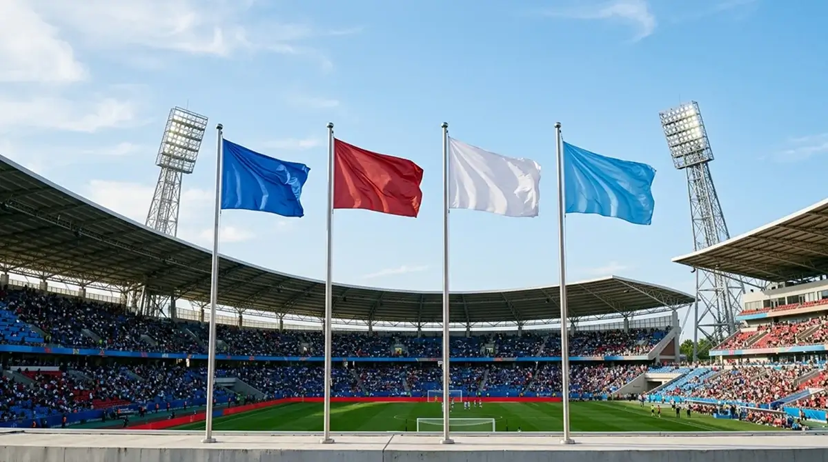 Four national flags flying together against a bright sky above a large stadium, floodlights and stands below